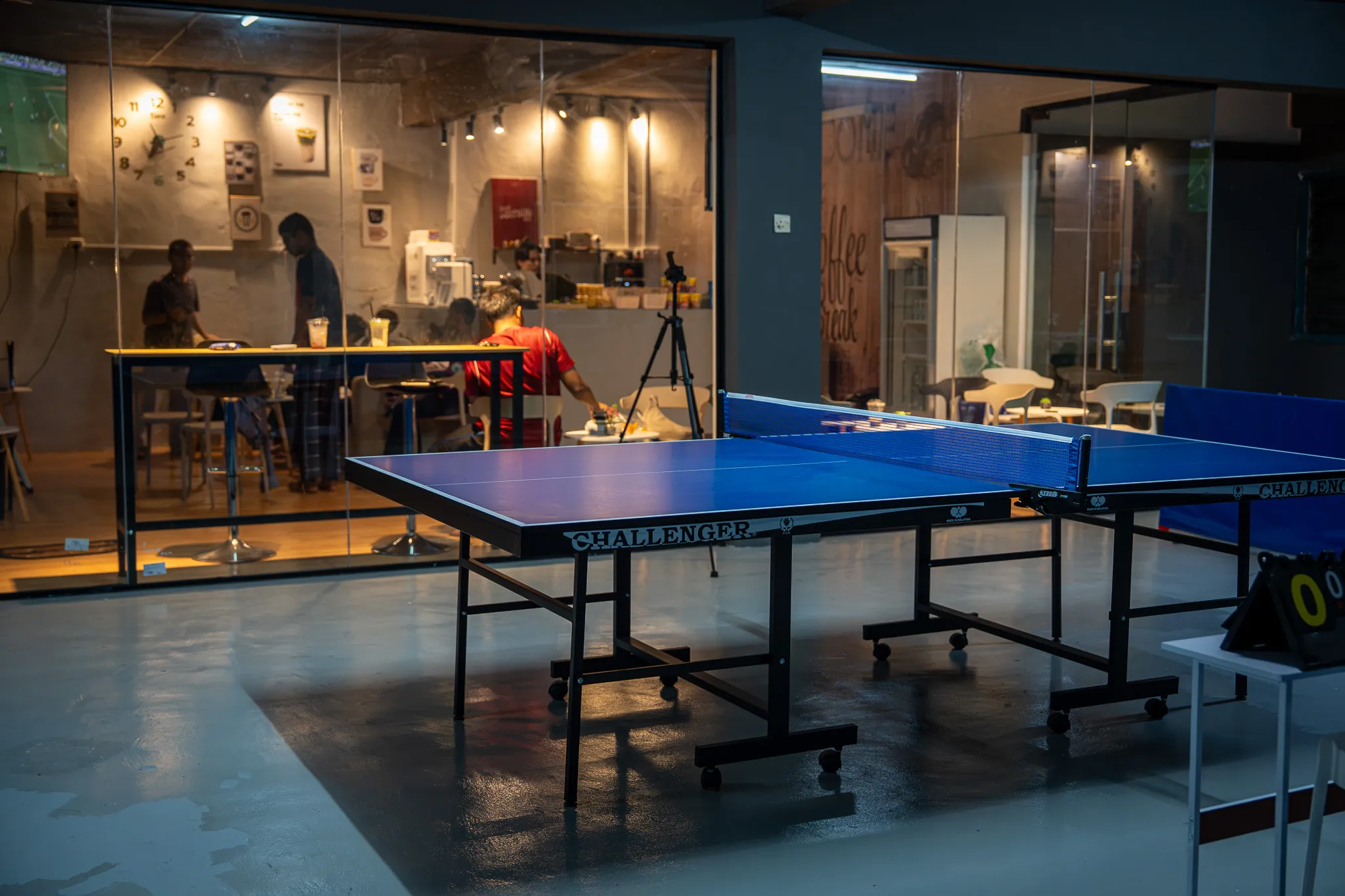 Table tennis table with the warm-lit cafe glowing behind glass at LekaPong